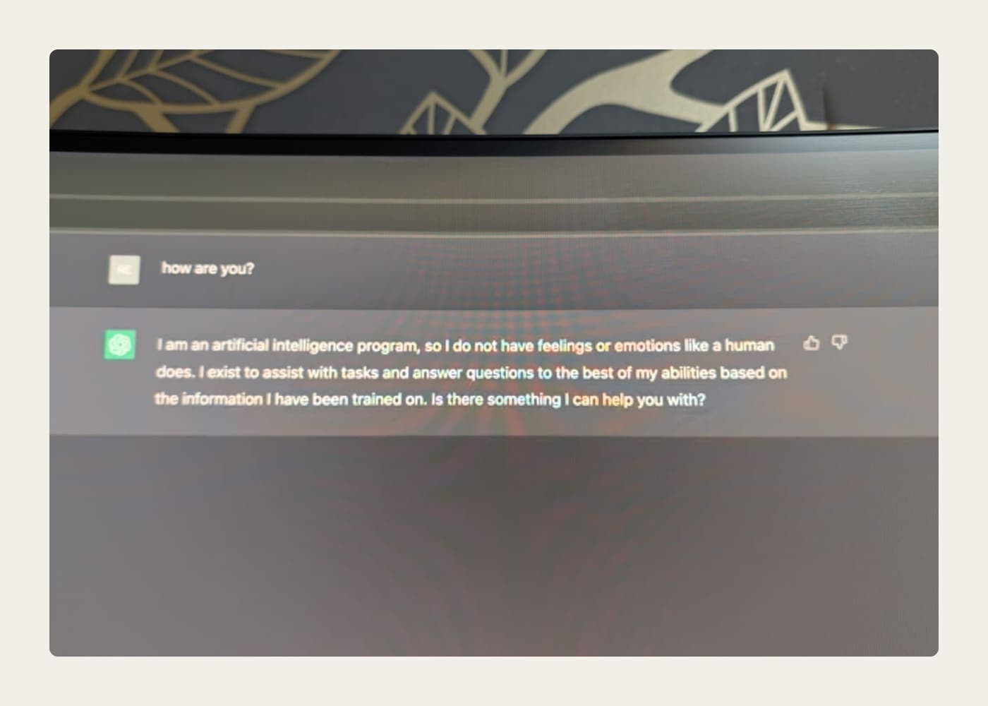 A photograph of an early ChatGPT exchange on a monitor: the question “how are you?” and a reply explaining it is an artificial intelligence program that does not have feelings and exists to help with tasks.
